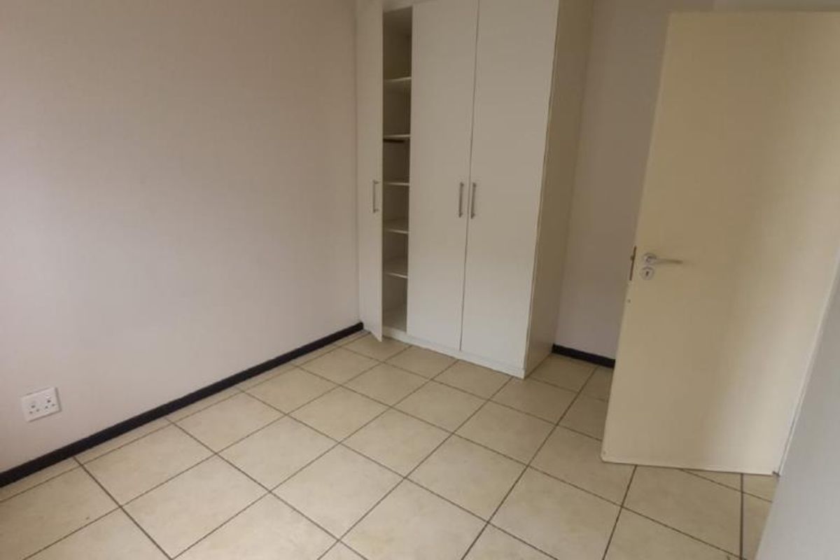 An empty bedroom featuring neutral tiled flooring and a white built-in wardrobe with shelving.