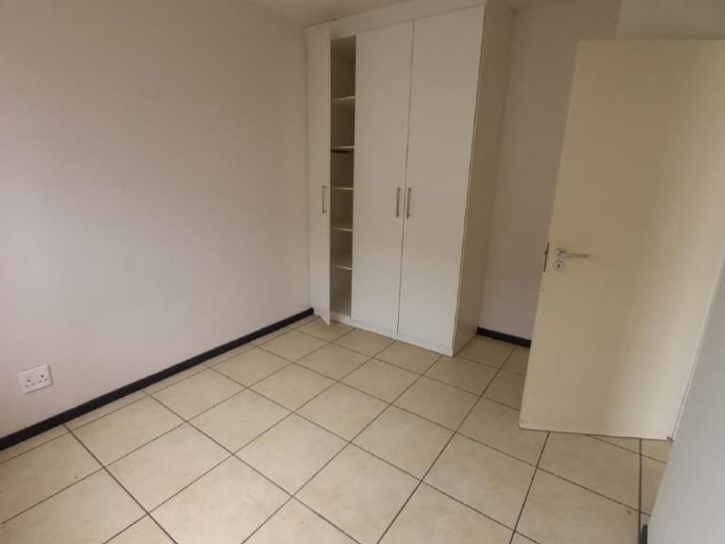An empty bedroom featuring neutral tiled flooring and a white built-in wardrobe with shelving.