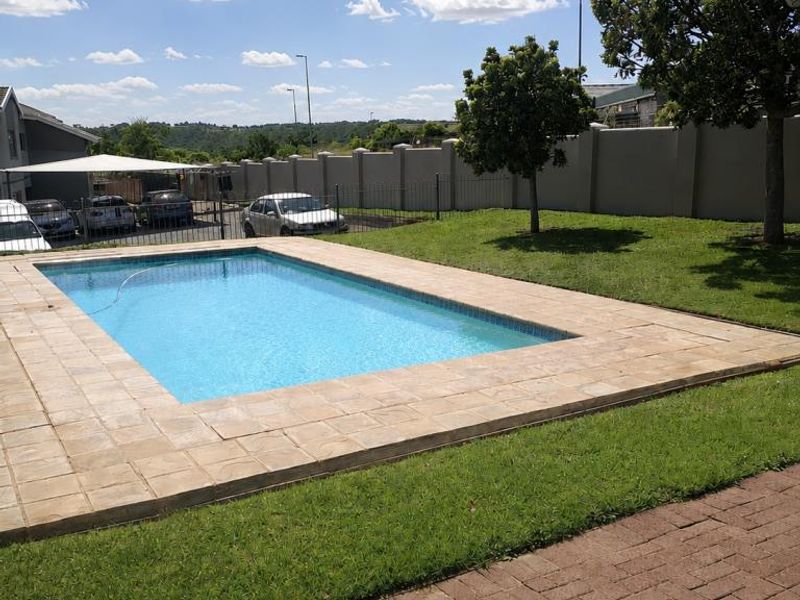 A well-maintained outdoor swimming pool area featuring a paved surround, manicured lawn, and secure boundary walling.