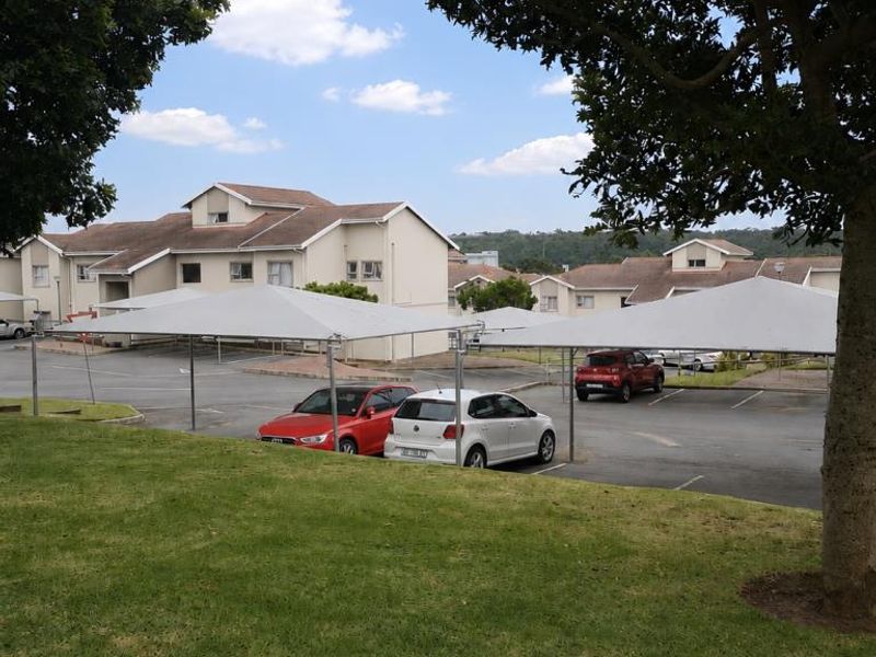 Exterior view of the apartment complex featuring paved parking bays with shade cloth carports and well-maintained surrounding lawn areas.