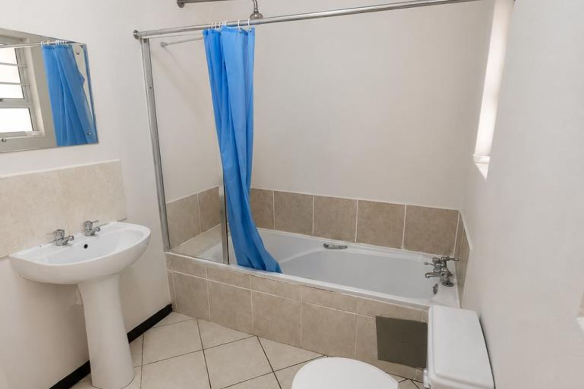 A functional bathroom featuring a pedestal washbasin, a bathtub with a shower attachment, and a standard toilet, finished with neutral wall and floor tiles.