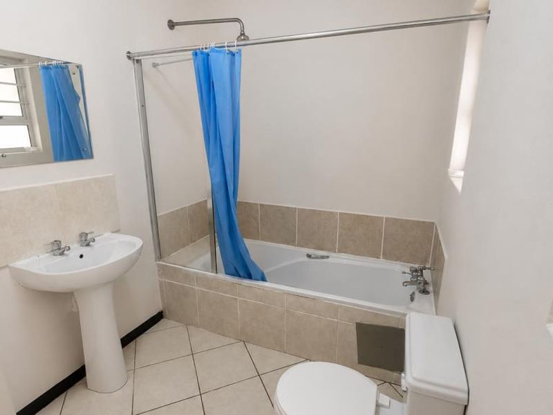 A functional bathroom featuring a pedestal washbasin, a bathtub with a shower attachment, and a standard toilet, finished with neutral wall and floor tiles.