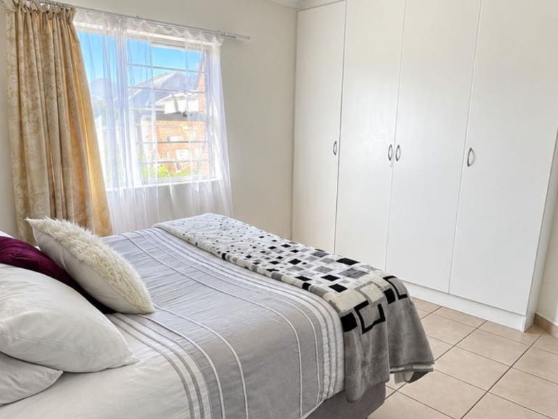 A bright bedroom featuring neutral tiled flooring and ample built-in cupboard storage, complemented by natural light from the window.