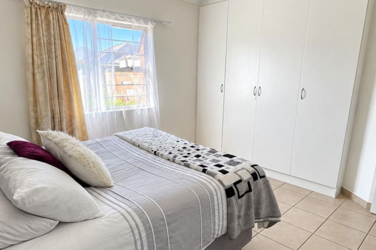 A bright bedroom featuring neutral tiled flooring and ample built-in cupboard storage, complemented by natural light from the window.