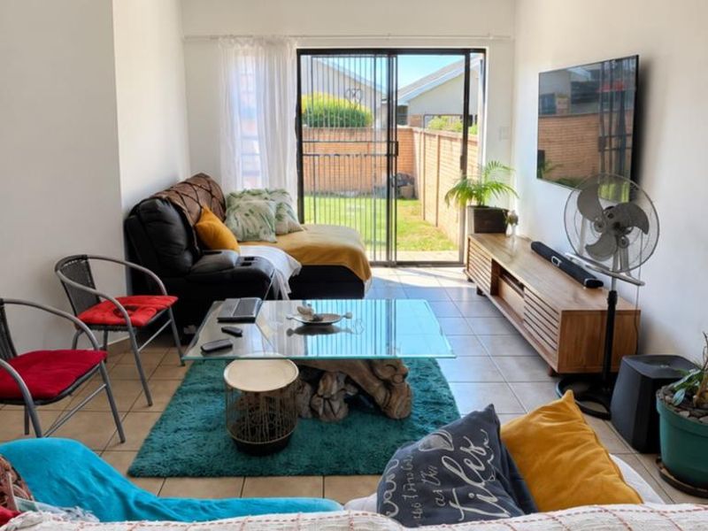 A bright living room featuring tiled flooring and a large sliding glass door that provides direct access to the rear garden area.