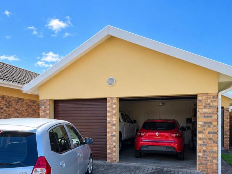 A double garage featuring a brick facade, a roller shutter door, and a paved driveway in a townhouse complex setting.