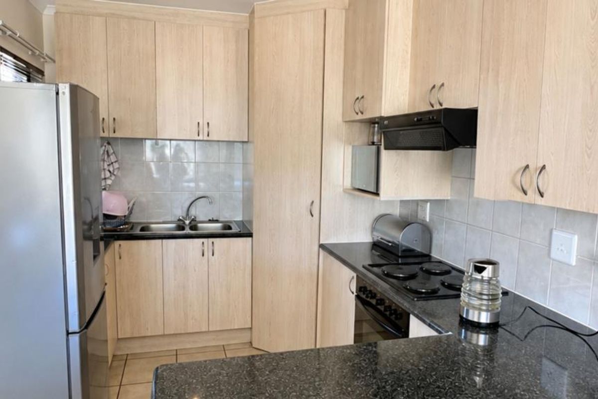 Functional kitchen featuring light wood-look cabinetry, dark granite countertops, tiled backsplash, and integrated appliances including an electric hob and oven.