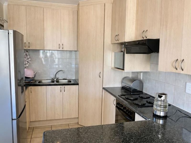 Functional kitchen featuring light wood-look cabinetry, dark granite countertops, tiled backsplash, and integrated appliances including an electric hob and oven.