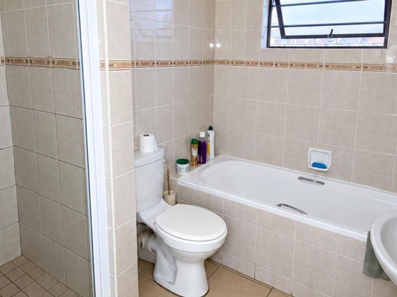 A functional bathroom featuring a separate shower enclosure, built-in bathtub, toilet, and washbasin with neutral wall and floor tiling.