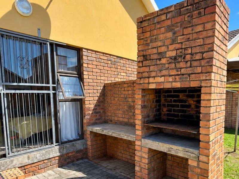 Outdoor patio area featuring a built-in brick braai with concrete prep counter, accessible via a sliding glass door with security gate.