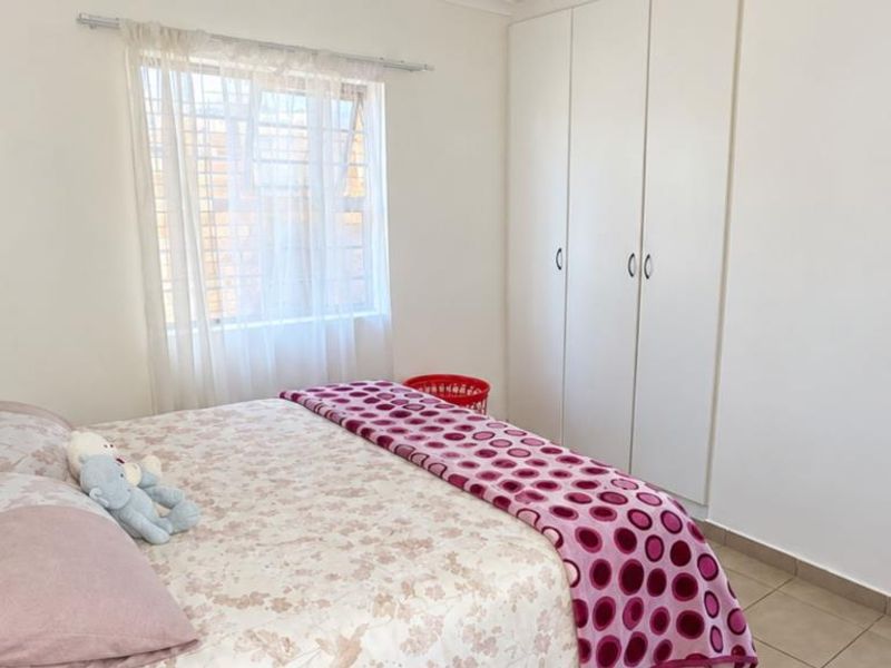 A functional bedroom featuring built-in cupboards, tiled flooring, and a window fitted with security bars, providing a clean and simple living space.
