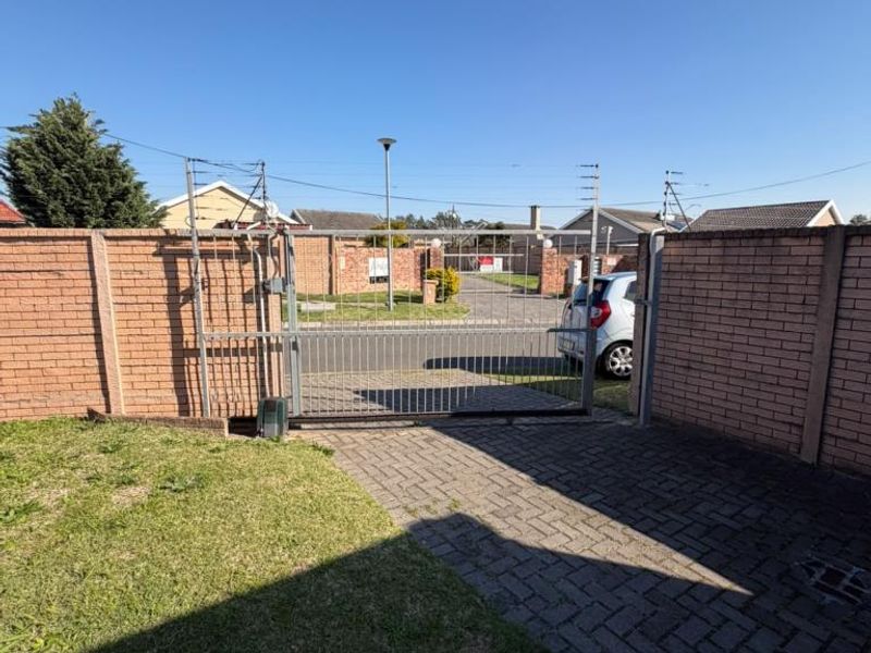Front entrance view of the property featuring a paved driveway, lawn area, and a secure metal sliding gate set within a brick boundary wall.