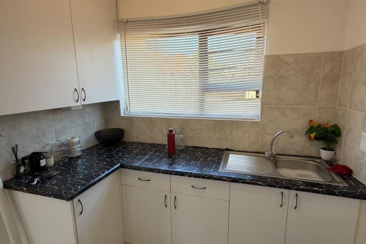 A functional kitchen area featuring white cabinetry, dark marble-effect laminate countertops, a stainless steel sink, and neutral tiled flooring.