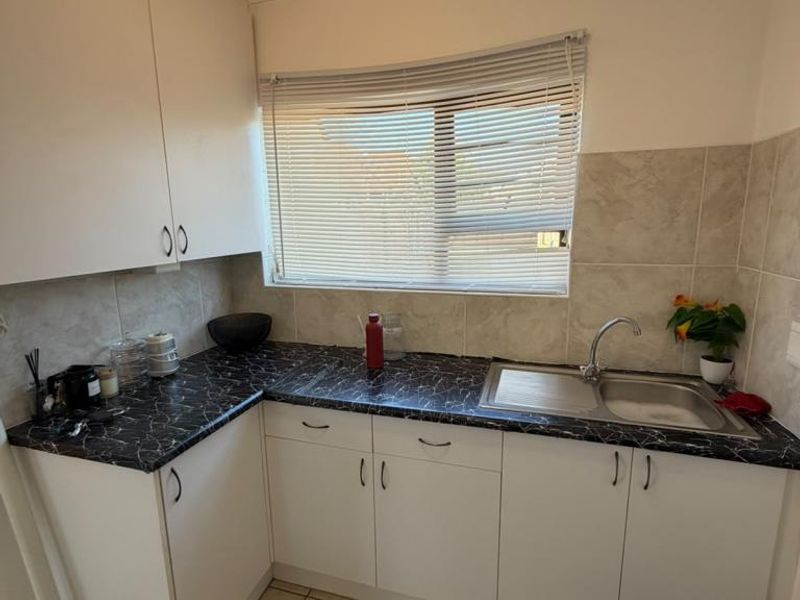 A functional kitchen area featuring white cabinetry, dark marble-effect laminate countertops, a stainless steel sink, and neutral tiled flooring.