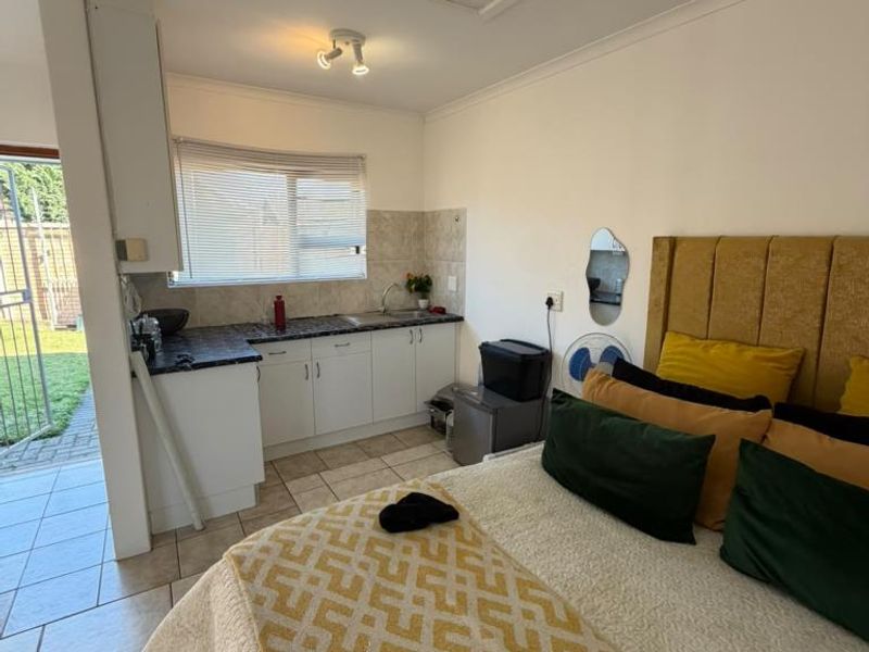 Open-plan studio apartment featuring a compact kitchenette with built-in cabinetry, tiled flooring, and direct access to an outdoor area.