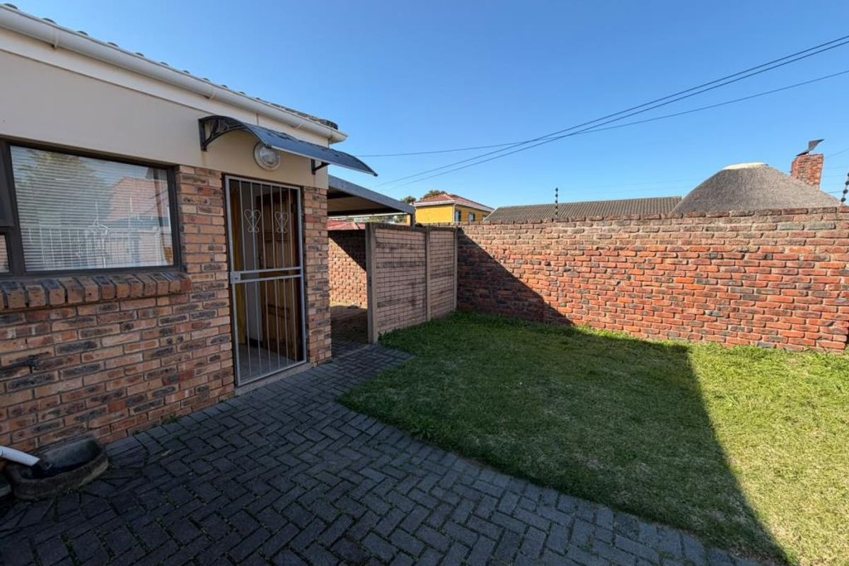 A private rear courtyard featuring a paved patio area, a small lawn, and a face brick boundary wall with a secure entrance.