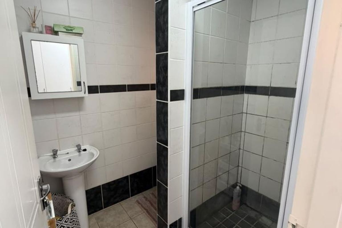 A functional bathroom featuring a pedestal basin, a glass-enclosed shower, and contrasting black and white wall tiling.
