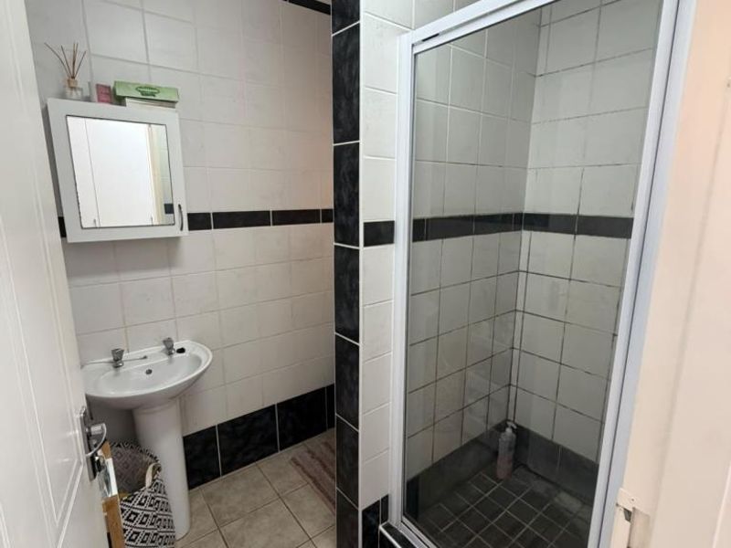 A functional bathroom featuring a pedestal basin, a glass-enclosed shower, and contrasting black and white wall tiling.
