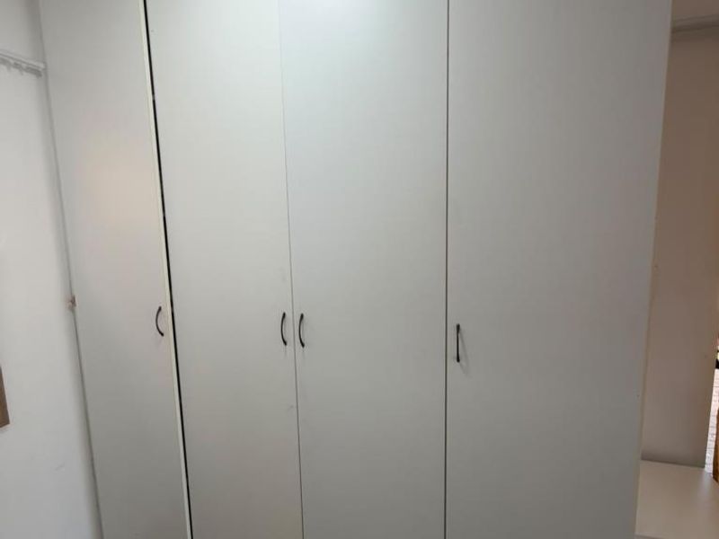 A bedroom featuring floor-to-ceiling white built-in cupboards and neutral tiled flooring, offering ample storage space.