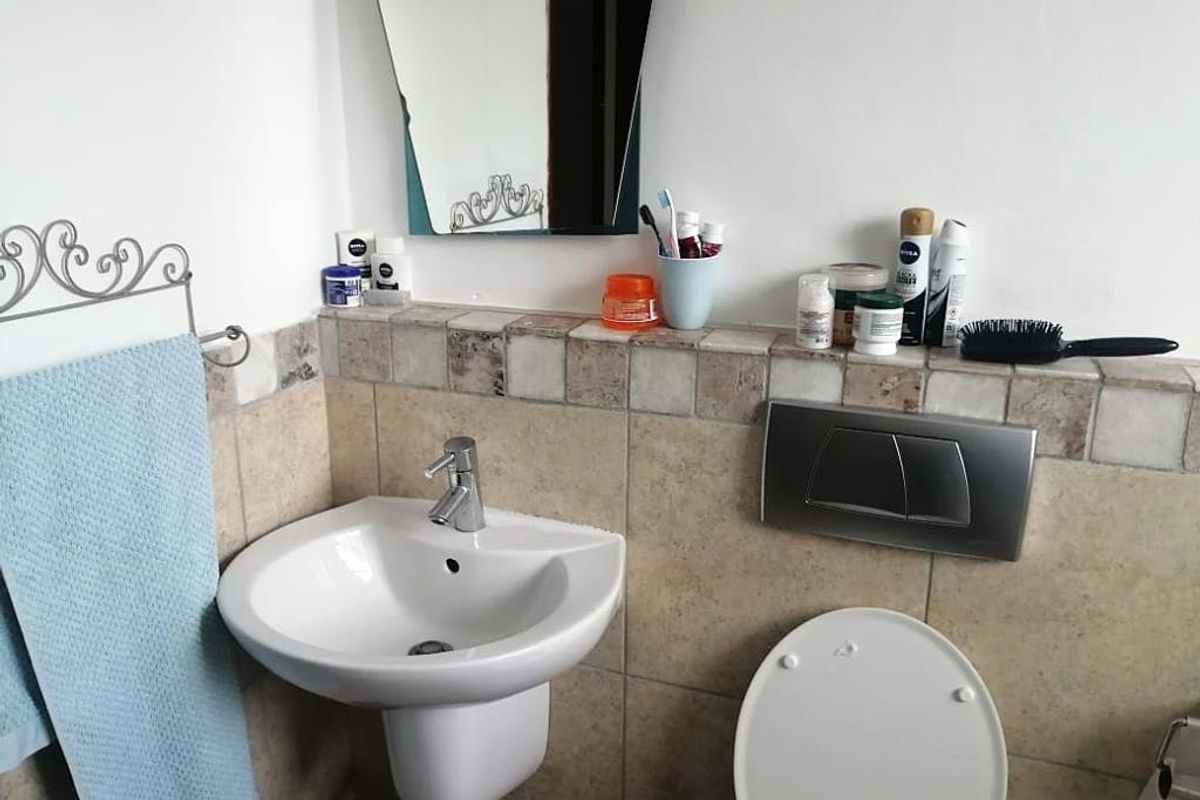 A compact bathroom featuring a wall-mounted basin, a concealed cistern toilet with a flush plate, and tiled splashback detailing.