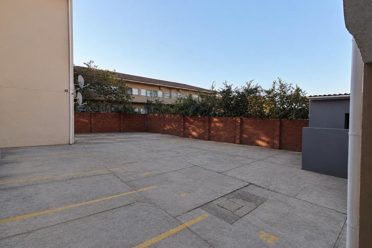 An open-air paved parking area featuring marked bays, enclosed by a perimeter brick wall within the apartment complex grounds.