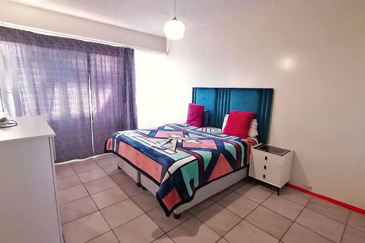 A bedroom featuring tiled flooring, a large window with curtains, and a central pendant light fixture.
