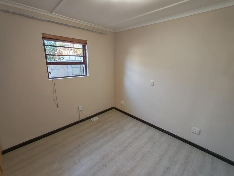 A vacant bedroom featuring light-toned laminate flooring, neutral walls, and a window fitted with security burglar bars.