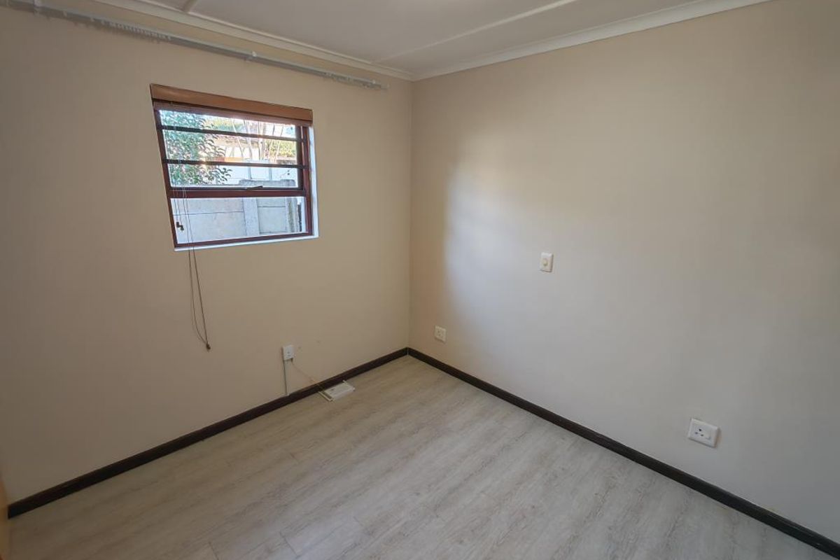 A vacant bedroom featuring light-toned laminate flooring, neutral walls, and a window fitted with security burglar bars.