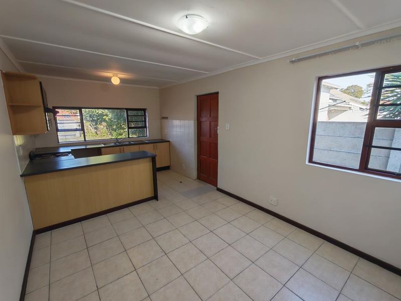 Open-plan kitchen and living area featuring tiled flooring, built-in cabinetry with laminate countertops, and natural light through aluminium-framed windows.