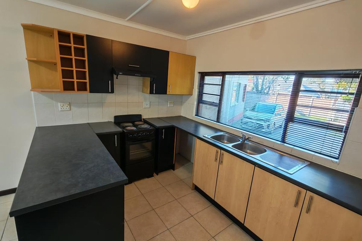 Functional kitchen featuring two-tone cabinetry, dark laminate countertops, a double sink, and a freestanding electric stove with an extractor fan.