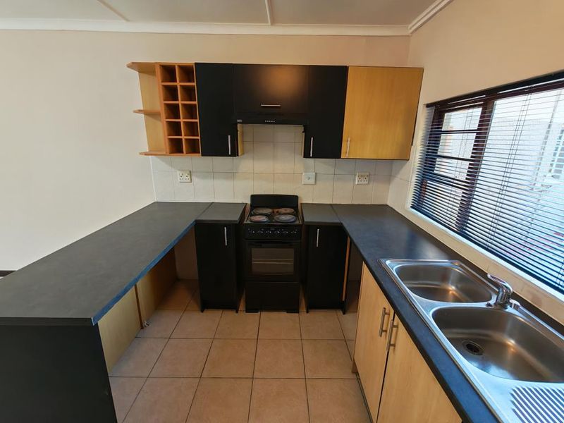 A functional kitchen featuring dark laminate countertops, built-in cabinetry with a wine rack, a freestanding stove with extractor, and a double stainless steel sink.