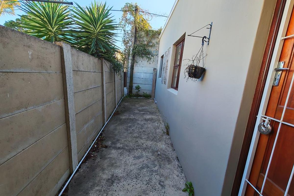 A narrow rear exterior walkway featuring a precast concrete boundary wall and a concrete path, providing access to the side of the apartment.