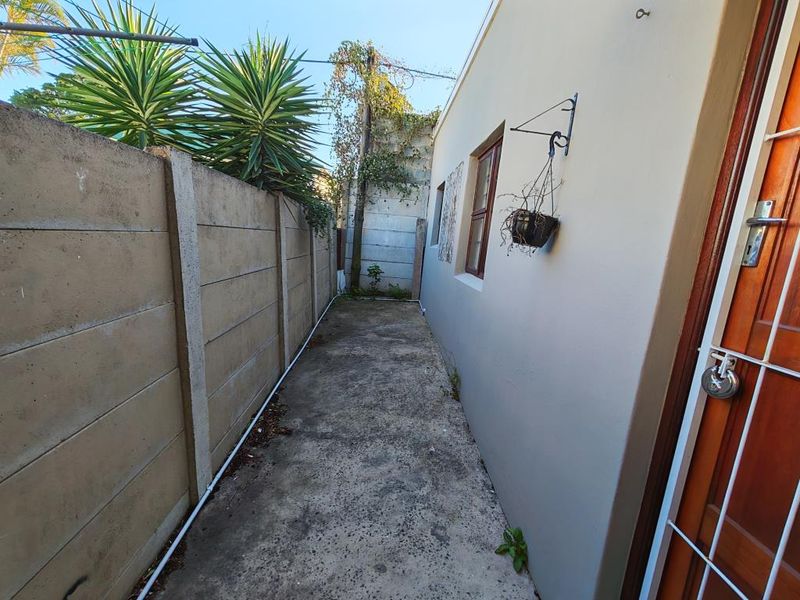 A narrow rear exterior walkway featuring a precast concrete boundary wall and a concrete path, providing access to the side of the apartment.