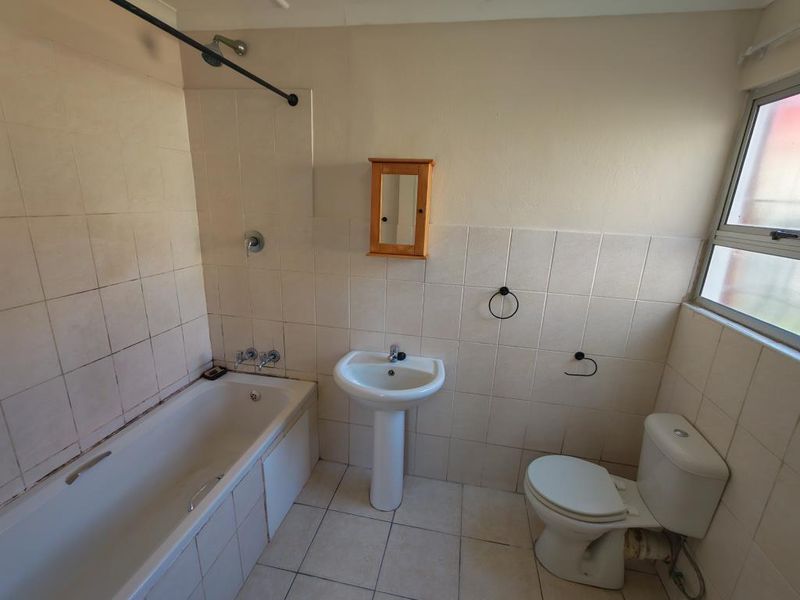 A dated bathroom featuring a bathtub, pedestal sink, and toilet with neutral wall and floor tiling, offering potential for modernization.