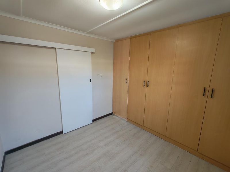 A clean, empty bedroom featuring light-toned laminate flooring and extensive built-in wooden cabinetry, offering ample storage space.