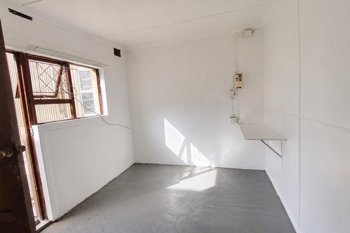 A compact, empty bedroom featuring a built-in wall shelf, security gate, and basic electrical fixtures, ready for renovation or staging.