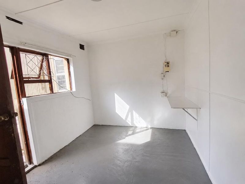 A compact, empty bedroom featuring a built-in wall shelf, security gate, and basic electrical fixtures, ready for renovation or staging.