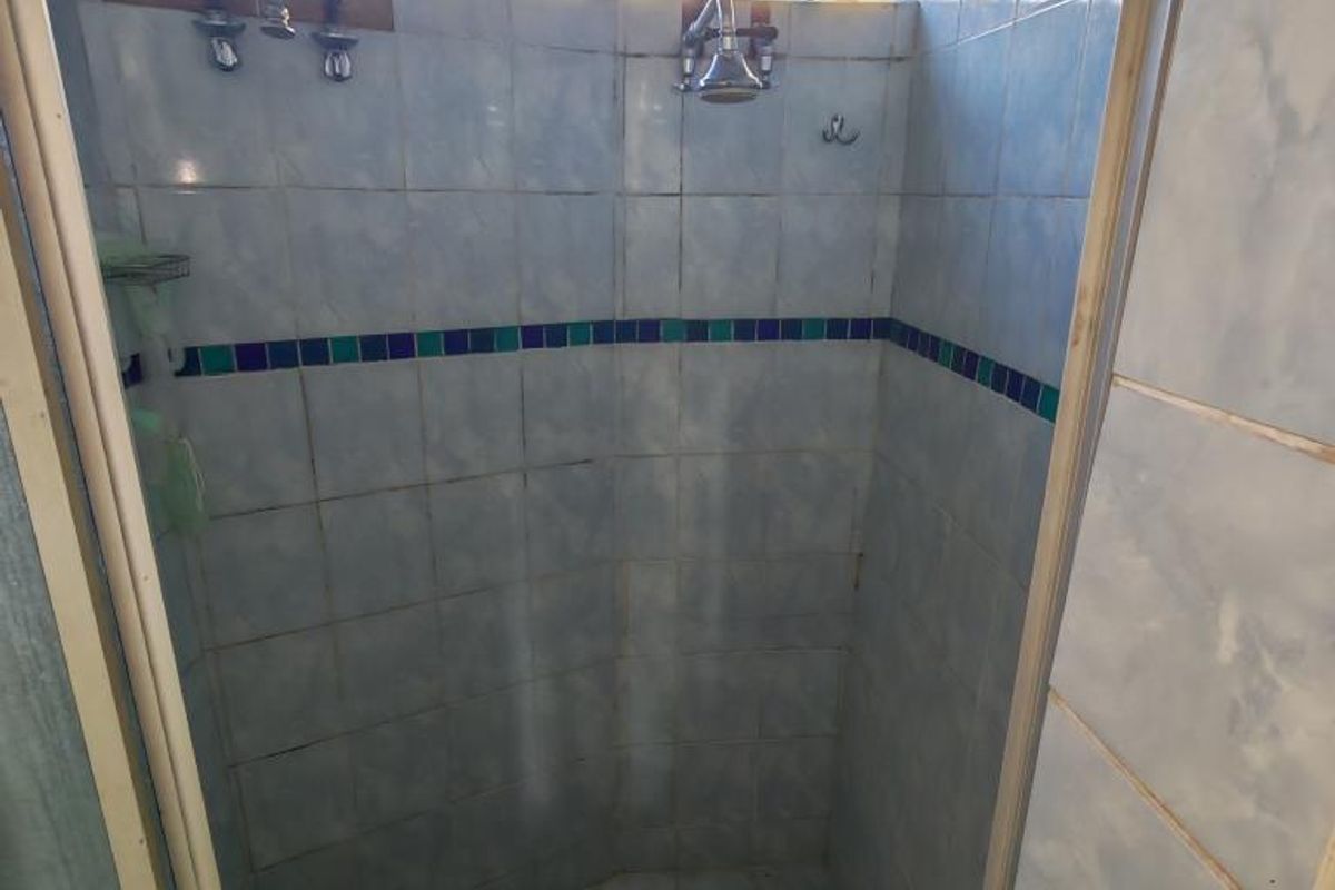 A dated shower enclosure featuring blue wall tiles, a glass block window, and exposed plumbing fixtures, requiring modernization to improve aesthetic appeal.