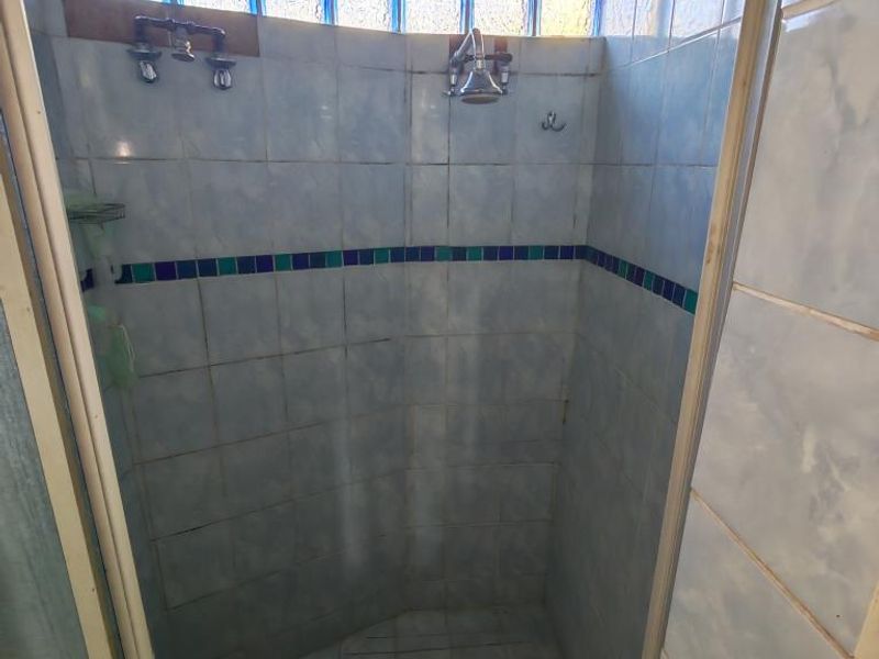 A dated shower enclosure featuring blue wall tiles, a glass block window, and exposed plumbing fixtures, requiring modernization to improve aesthetic appeal.