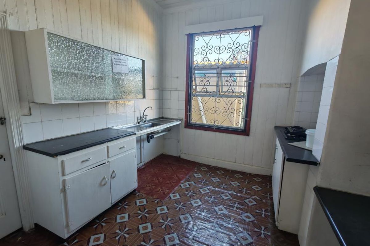 A dated kitchen featuring built-in cabinetry, a stainless steel sink, and tiled splashbacks, requiring modernization and cosmetic updates to improve functionality and aesthetic appeal.