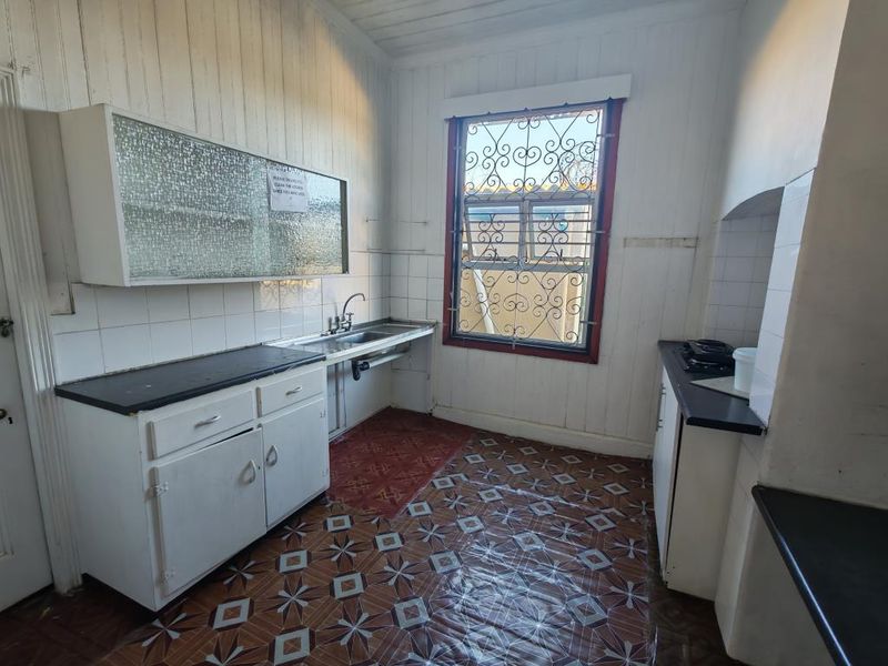 A dated kitchen featuring built-in cabinetry, a stainless steel sink, and tiled splashbacks, requiring modernization and cosmetic updates to improve functionality and aesthetic appeal.