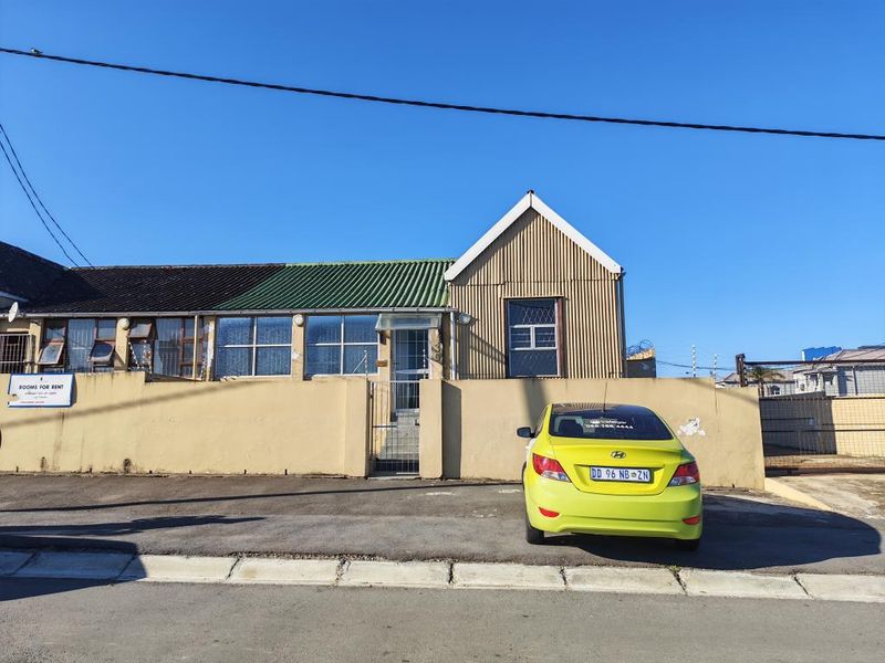 Front exterior view of a single-story apartment building featuring a corrugated metal roof, perimeter wall with security gate, and electric fencing.