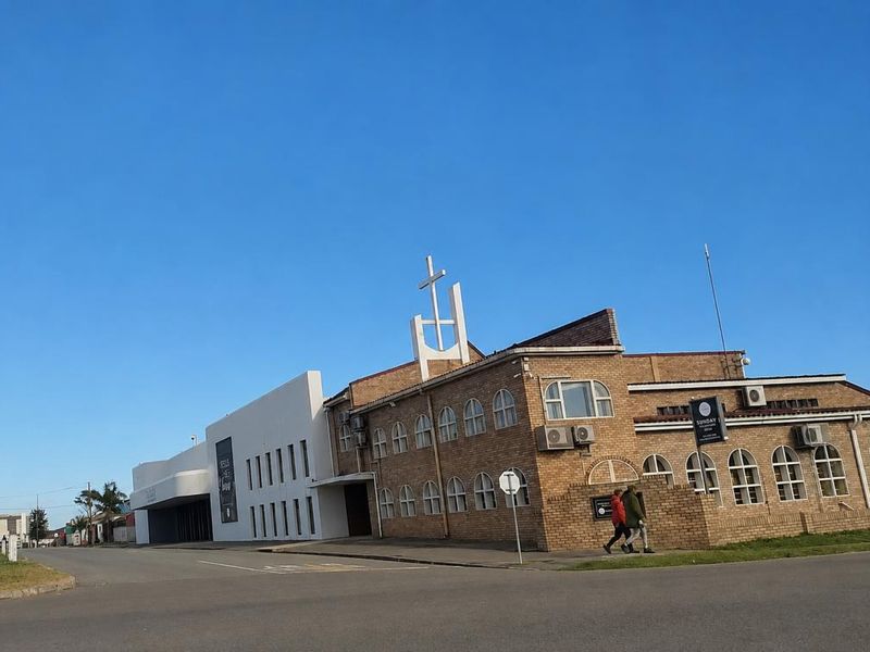 Exterior view of a building featuring a brick facade, arched windows, and a prominent cross structure, situated on a street corner.