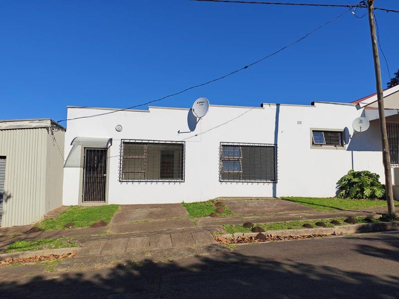 Front exterior view of the apartment building featuring a concrete driveway, security bars on windows, and a security gate at the entrance.