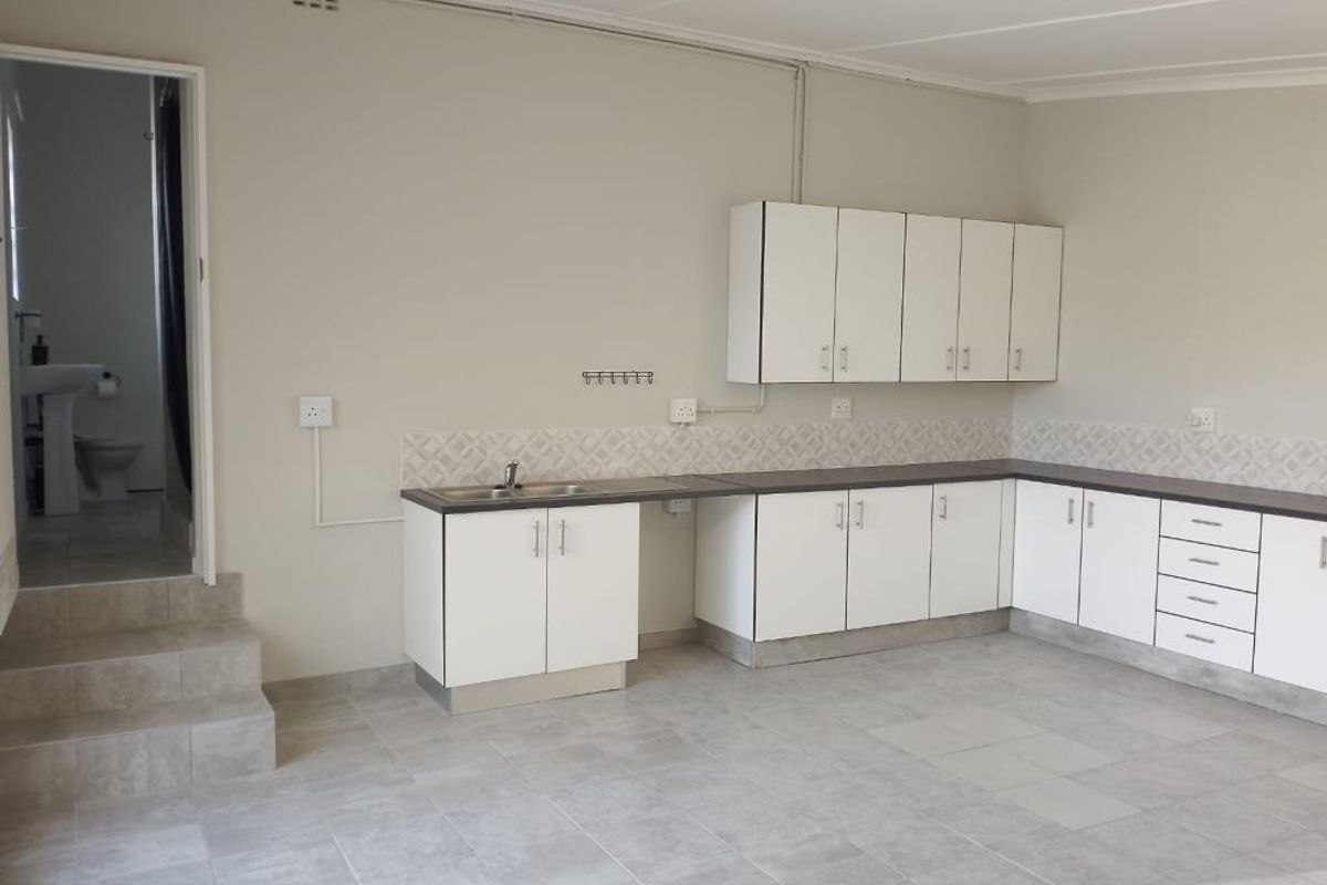 A clean, empty kitchen featuring white built-in cabinetry, dark laminate countertops, tiled backsplash, and tiled flooring, with an adjacent doorway leading to a bathroom.