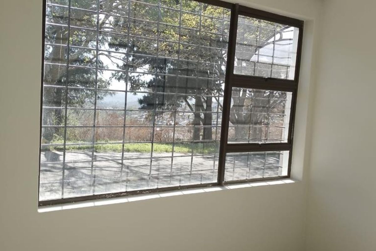 A bright, empty bedroom featuring tiled flooring and a large window with security bars, offering a pleasant view of the surrounding area.