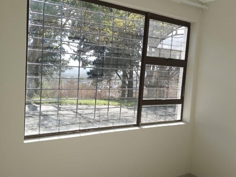 A bright, empty bedroom featuring tiled flooring and a large window with security bars, offering a pleasant view of the surrounding area.