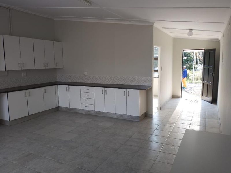 A functional, empty kitchen featuring white built-in cabinetry, dark laminate countertops, and neutral tiled flooring with direct access to the exterior.