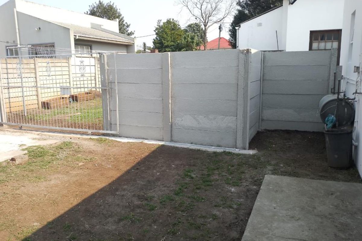 A rear exterior view of the property featuring a precast concrete boundary wall, a metal sliding gate, and an unlandscaped yard area.