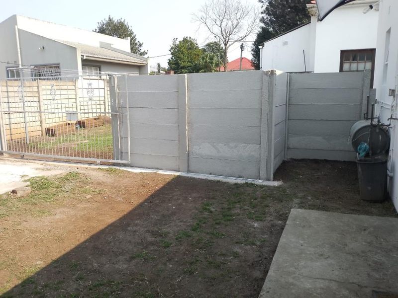 A rear exterior view of the property featuring a precast concrete boundary wall, a metal sliding gate, and an unlandscaped yard area.